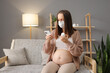 Unhealthy Caucasian brown haired pregnant woman treating her grippe symptoms at home using mobile phone for searching information about taking pills