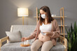Sick ill unhealthy Caucasian pregnant woman sitting on sofa at home holding tablets taking care of her health during pregnancy flu taking glass of water