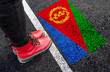 a woman with a boots standing on asphalt next to flag of Eritrea and border

