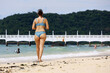 Slim woman in bikini walking by the sand on tropical beach. Sea coast, vacation on tourist resort