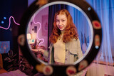 Fototapeta  - Portrait of stylish teen girl standing in her room posing for camera, through circle lamp medium shot