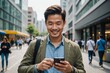© ThomasLENNE - An asian man in modern city center checking his smart phone and smiling