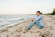 Portrait of stylish male enjoying amazing view. The handsome man joyfully walks near sea and looks at side. Young traveler man sitting in beach ocean and enjoying summer day on vacation. Side view.