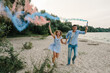 Happy married couple holds hands smoke bomb. Man and woman having fun running on sand and holding blue and red, pink color smoke bombs and looking at camera on beach. Baby shower. Twins:  boy and girl