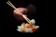 Hand Holding Chopsticks With Rice and Vegetables on Dark Background