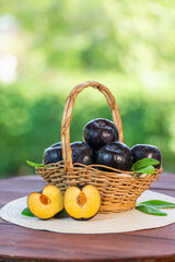 Wall Mural - fresh black plum fruit in bamboo basket on wooden table in garden, fresh black plum with slices on b