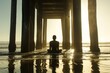 A serene silhouette of a person meditating under a wooden pier with the setting sun casting a warm glow
