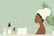 A female is seated in a bathtub with a towel wrapped around her head. She is engaged in personal skincare routines in a bathroom setting