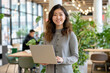 © 수동 김 - A photo of an attractive asian woman standing in the middle, smiling and holding her laptop computer while dressed for work in business casual attire with shoulder length curly hair