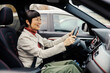 A middle aged japanese woman driving her car with hands on steering wheel.
