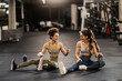 Two sporty girls sitting on a gym floor and taking a break after workout.