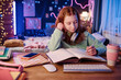 © AnnaStills - Medium shot of Caucasian girl with red hair sitting at desk in her room doing school homework in evening, copy space