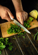 Chef hands use a knife to cut green parsley on a cutting board to prepare a vitamin salad. Delicious peasant food. Copy space
