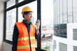 A young engineer stands with a walkie-talkie talking to a team of coordinating engineers at a construction site.