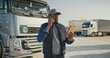 Portrait of african american worker talking by phone in background parked truck vehicles. Truck driver holding tablet, and checking route for new destination. Transportation service.