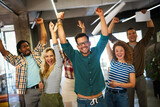 Fototapeta  - Happy young successful business team celebrating a triumph with arms up in startup office.