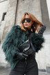 stylish beautiful glamorous woman with sunglasses in a fashion shaggy jacket with a handbag walks in the city near a vintage building