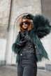 Glamorous beautiful stylish girl model with cool sunglasses in a fashion shaggy jacket with a black handbag with gloves posing in the city near a vintage building