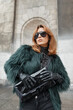 Cool stylish glamorous woman model with cool sunglasses in fashionable clothes with shaggy jacket with gloves and handbag in the city