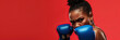 Close-up of intense female boxer with blue gloves poised to strike against a striking red background, exuding focus and determination. Banner with copy space.