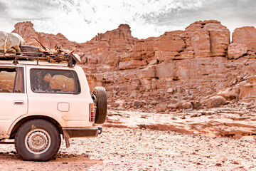 Rear side view of a 4x4 car loading package and wood in the Sahara desert of Tadrart Rouge. Parked in the reg with dry stones in the Sahara desert, rocky mountain with cloudy sky in the background.