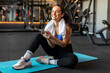 © Home-stock - Sports lifestyle. Lady in sportswear uses cellphone during workout, resting and smiling at camera. She posts photos from the training on social media