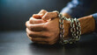 Close-up of male hands in chains against a dark backdrop, evoking confinement, struggle, and oppression. Moody tone, isolated focus on hands.