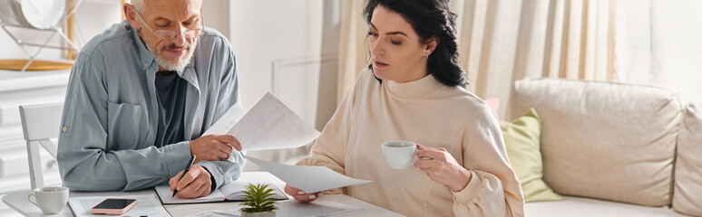 A man and woman sit at a table, surrounded by papers, engaged in a serious discussion.