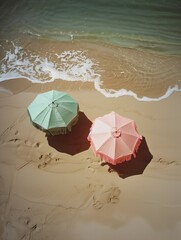 A photo of two pastel  beach umbrellas on the sand, one in sage green and another pink with fringes, taken from above with natural lighting. Romantic summer background. 