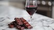 A simple composition featuring a glass of red wine and a piece of dark chocolate on a marble surface.
