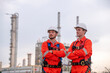 Engineer survey team wear uniform and helmet stand workplace checking blueprint project , radio communication and engineer box inspection work construction site with oil refinery background