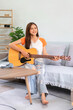Concept of relaxation with music, Young woman sit on couch to playing music with acoustic guitar