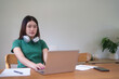 Young asian student women wearing headphone in her neck and researching information for learning knowledge remote education from home while studying and watching lecture webinar in online class