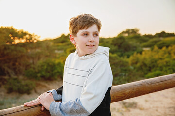 Happy cheerful teenager standing on beach at sunset. happy preteen boy smiling at the camera. Kid on family vacation at the sea.