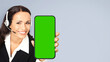 Call Center Service. Customer support, sales phone agent in headset show cellphone mobile green chroma key mockup screen. Business woman hold smartphone, isolated against grey gray background.