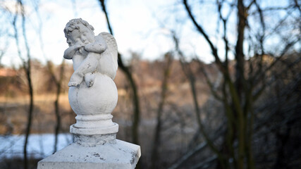 Wall Mural - angel statue in the park. little boy with wings. cupid statue in autumn park. figurine for design, marble sad angel sitting on a ball. blurred natural background. 