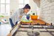 Cheerful young smiling woman washing table with rag and detergent at the kitchen disinfecting her apartment. Girl housewife cleaning surface of counter. Domestic chores, housework concept.