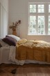 bedroom with white walls, parquet floor and window, bed is made up with yellow bedding