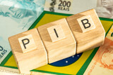 Fototapeta  - The word PIB (Gross Domestic Product) written on wooden cubes with some Brazilian real banknotes on yellow, green and blue national symbols of Brazil. Brazilian Portuguese language