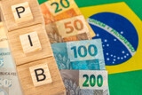 Fototapeta  - The word PIB (Gross Domestic Product) written on wooden cubes with Brazilian real money in yellow, green flag of Brazil. Brazilian Portuguese language