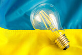 Fototapeta  - A glowing light bulb lying in the middle of the Ukrainian flag, Concept, Energy problems and energy prices in Ukraine