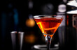 Orange alcoholic hard cocktail drink with scotch whiskey, vermouth and liquor in martini glass, dark bar counter background close-up