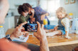 © Marko Geber - Family baking together in kitchen with mother and children making dough and father taking a photo