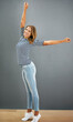 Woman, happy and home fashion or relax, casual and carefree or stretch for freedom and smile. Standing, grey wall and portrait in jeans with confident girl, weekend and comfort style or outfit