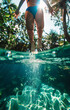 Underwater view of young woman jumping into swimming pool at tropical resort