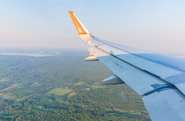 View of airplane wing, blue skies and green land during landing. Airplane window view.