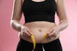 Woman measuring belly with tape on pink background, closeup. Overweight problem