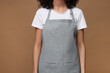 Woman wearing kitchen apron on brown background, closeup. Mockup for design