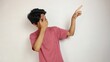 Young Asian man poses pointing upwards while closing his eyes on an isolated white background