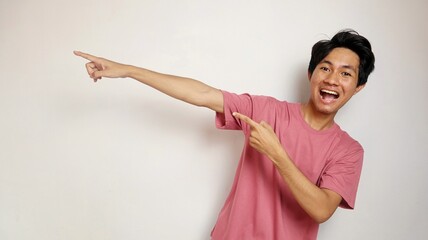 Wall Mural - young handsome Asian man happy, cheerful and enthusiastic posing pointing to the side with an isolated white background